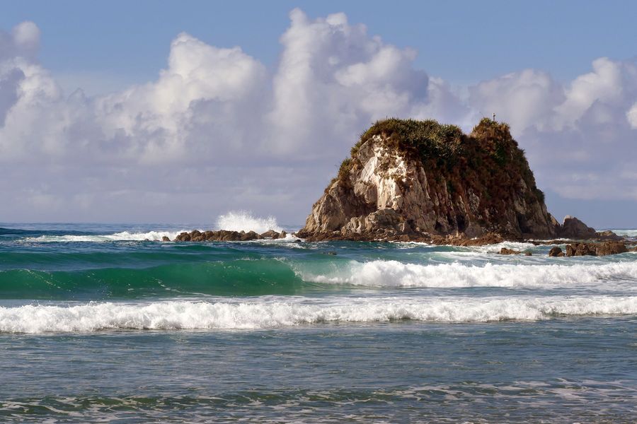 Surf breaking on the sand at Mangawhai Heads, with a large rock stack offshore.