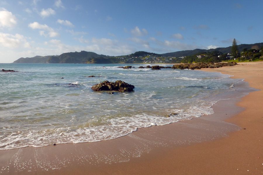 Small waves washing onto golden sand at Langs Beach, with houses and a headland across the bay.
