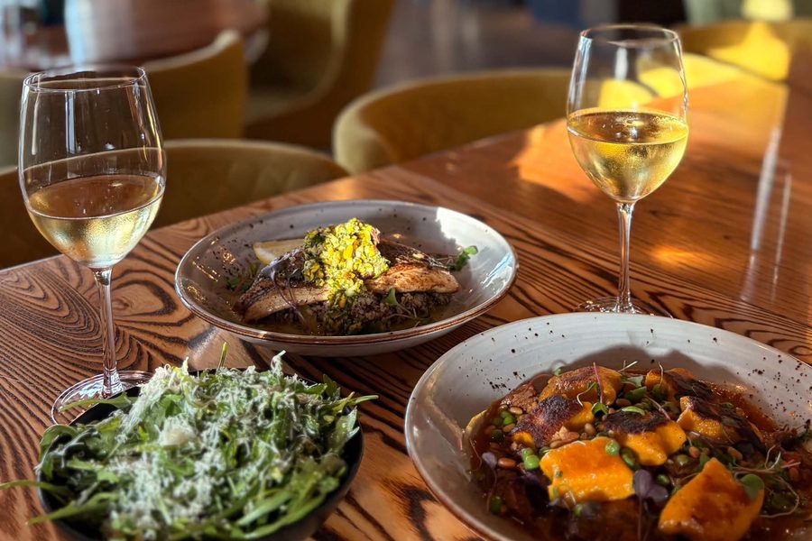 Two dinner plates, a salad and two glasses of white wine on a wooden table in the dining room at The Local.