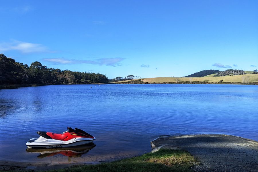A jet ski pulled up on the edge of a deep blue lake, with bush and farmland on the far shore.